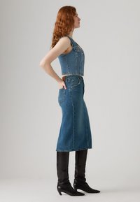 Denim jurk met een aansluitend lijfje en A-lijn rok, uitgevoerd in blauwe kleur, met knopen aan de voorkant en twee zijzakken, gecombineerd met kniehoogte zwarte laarzen.