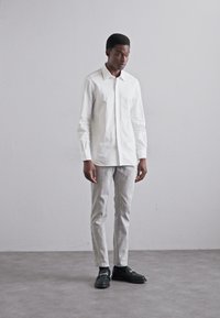 White long-sleeve shirt paired with light grey trousers. The outfit features a classic design, with no visible patterns or embellishments.