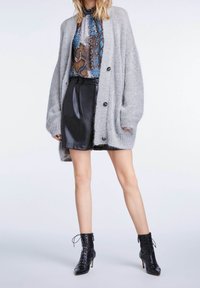 Cardigan grigio lavorato a maglia con grandi bottoni, indossato sopra una maglietta con stampa serpente, abbinato a una gonna nera in pelle sintetica e stivaletti neri con lacci.