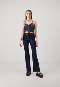 Prilagođeni tamnoplavi crop top s nabranim detaljima i uzicom, uparen s tamnoplavim širokim trapericama i masivnim crnim platformama.