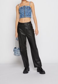 Top de mezclilla cortado con cierre de cremallera, pantalones de piel negra de pierna ancha, botas negras de suela gruesa y un bolso de cuadros azules con correa de cadena.