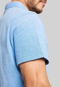 Himmelblaues Polo-Shirt mit kurzen Ärmeln, aus weichem Stoff. Details umfassen einen klassischen Kragen und sauber genähte Kanten.