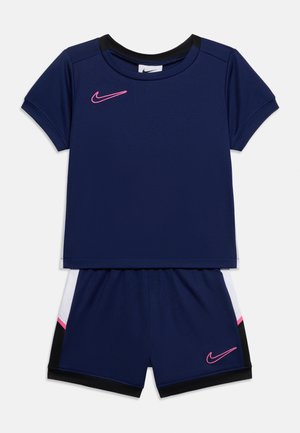 Tamsiai mėlyni sportiniai šortai ir trumpomis rankovėmis marškinėliai su rožiniais Nike swoosh logotipais ir baltais, juodais bei rožiniais šonų akcentais.