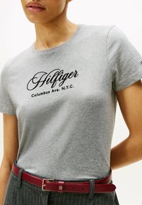 Grå kortærmet t-shirt med sort broderet 'Hilfiger' logo og teksten 'Columbus Ave. N.Y.C.', båret med et rødt læderbælte.