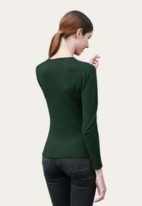 Haut ajusté à manches longues de couleur vert foncé avec un col rond et une texture lisse, associé à un jean en denim foncé, vu de dos.