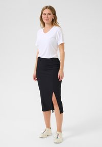 T-shirt blanc à manches courtes en V associé à une jupe noire jusqu'aux genoux avec une fente sur le côté. Des baskets légères complètent la tenue.