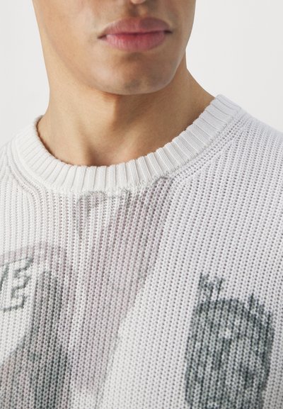 Weißer Strickpullover aus strukturiertem Material, mit einem gerippten Ausschnitt und einem abstrakten grauen Grafikdesign auf der Vorderseite.