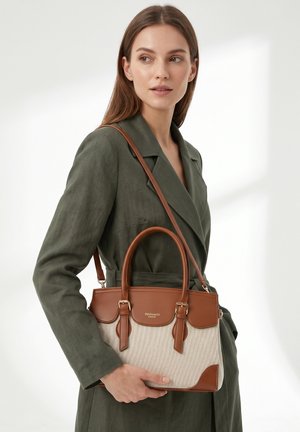 Vrouw in olijfgroene jas houdt een beige en bruine leren handtas met dubbele handvatten en een schouderriem vast.