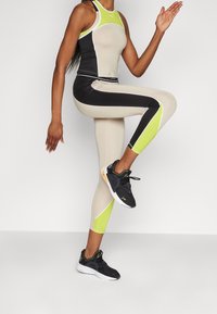 Completo fitness caratterizzato da una combinazione di colori nero, beige e verde neon. Adatto, realizzato in materiale elasticizzato, con design a schiena scoperta e scarpe da ginnastica.