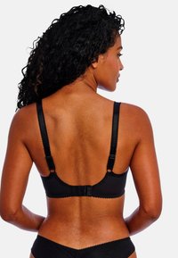 Soutien-gorge noir avec des bords festonnés, des bretelles réglables et une fermeture à crochets au dos. Texture lisse.