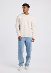 Beige crewneck sweater paired with light blue jeans. The sweater has a soft texture; jeans feature a relaxed fit and classic five-pocket design.