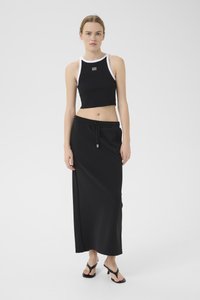 Must have mustar šortse musta tank top valge ääre ja logoga, koos musta pikkade seelikutega, millel on paeltega vöökoht. Mudel kannab musti flip-flop jalatseid.