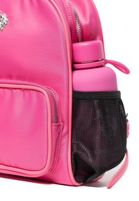 Różowy plecak z nylonu z główną komorą na zamek, boczną siateczkową kieszonką na różową butelkę na napój oraz gładką fakturą z detalem logo.