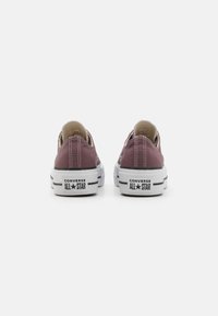 Converse All Star niske tenisice u tamnoj burgundijskoj platnu, s bijelim gumene potplate, kontrastnim šavovima i logotipom brenda na peti.