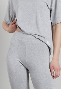 Grijze katoenen t-shirt met korte mouwen en een gebogen zoom, gecombineerd met grijze high-waisted legging. Bevat een klein logo-label aan de zijkant.