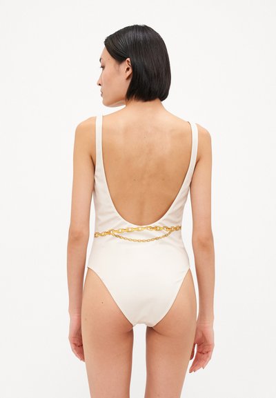 Maillot de bain une pièce blanc avec un dos plongeant et un détail en chaîne dorée au niveau de la taille. Texture lisse, fines bretelles.