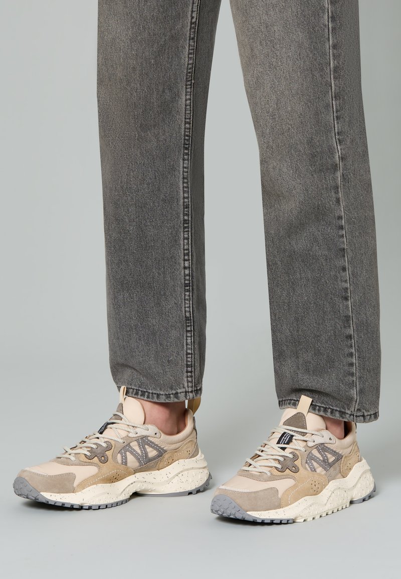 Sneakers beige e grigi con un mix di materiali scamosciati e in rete, silhouette robusta, suola testurizzata e dettagli dei lacci.