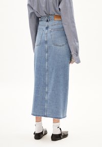 Denim midi rok in lichtblauw met een hoge taille, achterzakken en een onafgewerkte zoom. Gecombineerd met een gestreept shirt en zwarte instappers.