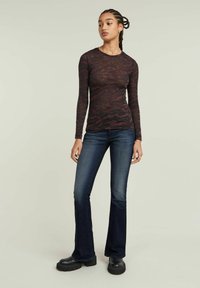 Long-sleeve top in dark red and black camouflage pattern, made of lightweight fabric. Paired with flared dark denim jeans and chunky black boots.