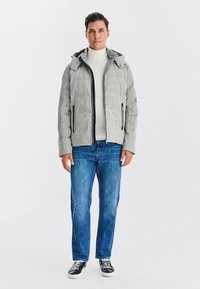 Szara kurtka z kapturem o pikowanej teksturze, czarnym zamkiem błyskawicznym i dwoma bocznymi kieszeniami, noszona na białym golfie i niebieskich dżinsach.