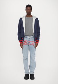 Marinejakke med grå foret hætte, grå skjorte, lyseblå jeans med rød hunde broderi og sorte klipklapper. Enkel, afslappet design.