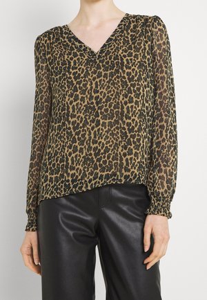 Femme portant un chemisier à manches longues imprimé léopard avec col en V, associé à un pantalon en cuir noir, montré des épaules jusqu'au milieu des cuisses.