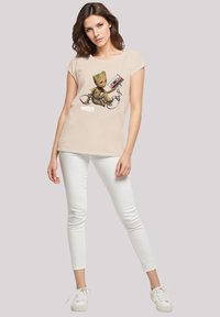 Light beige t-shirt featuring a graphic of a cartoon character holding a cassette tape, paired with white skinny jeans and white sneakers.