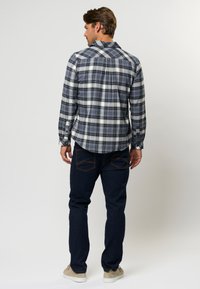 Mėlynos, baltos ir raudonos spalvų plaid ilgomis rankovėmis marškiniai, pagaminti iš šiek tiek tekstūruoto audinio; dėvimi su tamsiai mėlynomis džinsinėmis kelnėmis.