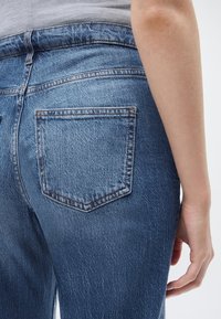 Κοντινό πλάνο ενός ατόμου που φοράει μπλε τζιν με ορατή πίσω τσέπη και μέρος του δεξιού του χεριού και μπράτσου.