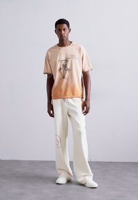 Kortærmet gradient T-shirt i fersken med palme grafik, parret med løse, creme-farvede bukser med en cirkulær detalje.