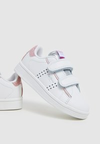 Sneakers bianchi con due cinturini in velcro, con accenti rosa e argento sul tallone e un motivo a stelle lungo il lato. Suola in gomma texturizzata.