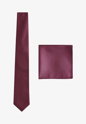 Egyszínű bordó színű selyem nyakkendő és hozzáillő zsebkendő finom texturált mintával, fehér háttéren.