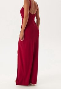 Robe maxi rouge à silhouette ajustée, bretelles spaghetti et fermeture éclair au dos. Dotée d'une fente latérale et d'une texture lisse et mate.