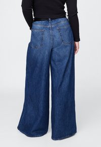 Džíny s širokými nohavicemi v tmavě modré barvě, s tradičním pětikapsovým designem a viditelným prošitím podél pasu a lemu.