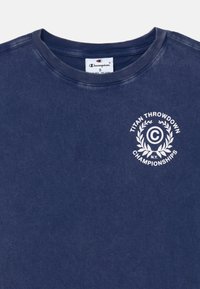 Námořnicky modré tričko s krátkým rukávem vyrobené z bavlny. Obsahuje bílé kulaté logo s nápisem "Titan Throwdown Championships" a designem vavřínu.