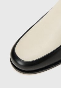 Μαύρο και κρεμ δερμάτινο παπούτσι με στρογγυλή μύτη, που διαθέτει λεία φινίρισμα και αντίθετες λεπτομέρειες στο κεντρικό ραφί.