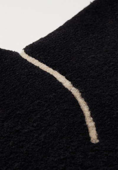 Zwarte textuurstof met een zachte, fuzzy uitstraling, voorzien van een opvallende beige gebogen lijn die het ontwerp benadrukt.