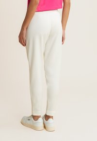 Joggers blancos en un corte tapered con una textura suave, cinturilla elástica y dobladillo ajustado. Combinados con zapatillas de tonos claros.