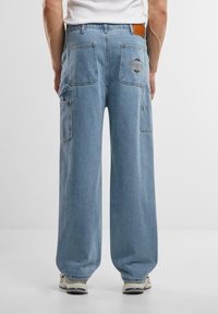 Lyseblå bred ben cargo bukser med fire store lommer og et brandet mærke på den bageste talje. Lavet af denimstof med en afslappet pasform.
