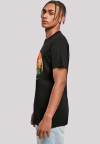 Black cotton t-shirt with a round neckline, featuring a colorful sunset and forest graphic on the front. Short sleeves, relaxed fit.