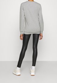 Sweat-shirt gris à manches longues, col rond et poignets côtelés, associé à des leggings noirs et des baskets blanches avec des accents crème.
