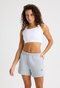 Sostén deportivo blanco con banda ancha y diseño de espalda nadadora, combinado con pantalones cortos de mezcla de algodón en gris claro que cuentan con una cinturilla elástica y bolsillos laterales.