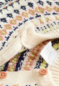 Cremefarvet strikket sweater med blomster mønstre i pastelfarver, ribbet krave og lyserøde knapper. "NEXT" mærket synligt indeni.