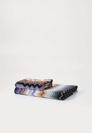 Asciugamani intrecciati multicolori con un motivo a zigzag. Presentano tonalità di viola, arancione, verde acqua e nero. Texture morbida, impilati su uno sfondo bianco.