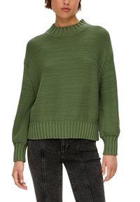 Groene gebreide trui met een gestructureerd patroon, ronde hals en ribbelmanchetten en -zoom. Gecombineerd met donkere jeans, wat zorgt voor een relaxte pasvorm.