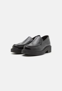 Scarpe slip-on nere in pelle con punta arrotondata, suola spessa in gomma nera e minimi dettagli di cucitura lungo i bordi.
