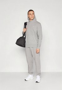 Grauer Hoodie mit Fronttasche, kombiniert mit passenden Sweatpants. Schwarze Reisetasche und weiße Turnschuhe. Schlichtes Design, weiches Material.