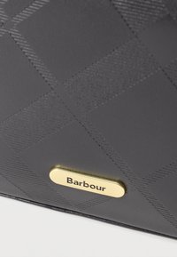 Fekete textúrájú táska gyémántmintával, arany színű fémtáblával, ami a "Barbour" nevet viseli. Simább, matt felület.