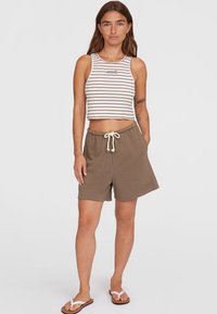 Gekürztes, gestreiftes Tanktop in Weiß und Braun, kombiniert mit braunen Shorts mit elastischem Bund und Kordelzug. Das Model trägt Flip-Flops.