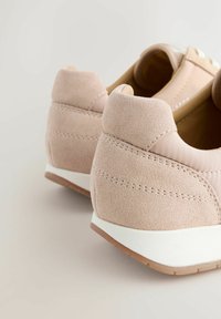 Chaussures de sport rose clair avec un mélange de dessus en daim et synthétique, talon rembourré, et semelle blanche texturée avec une prise en caoutchouc.